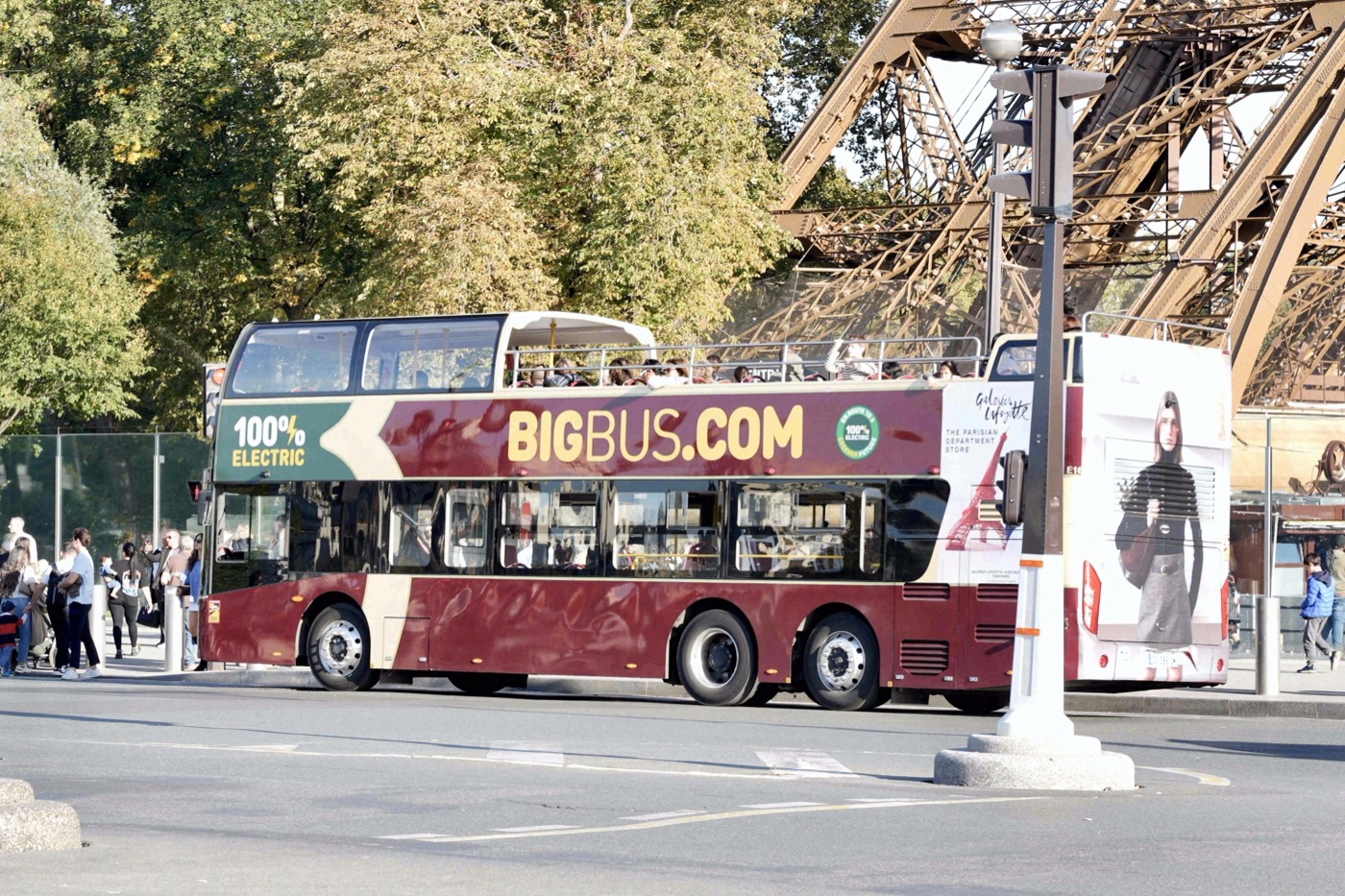 Ein roter Big-Bus-Touristendoppeldecker hält direkt neben den Stahlträgern des Eiffelturms an einer Pariser