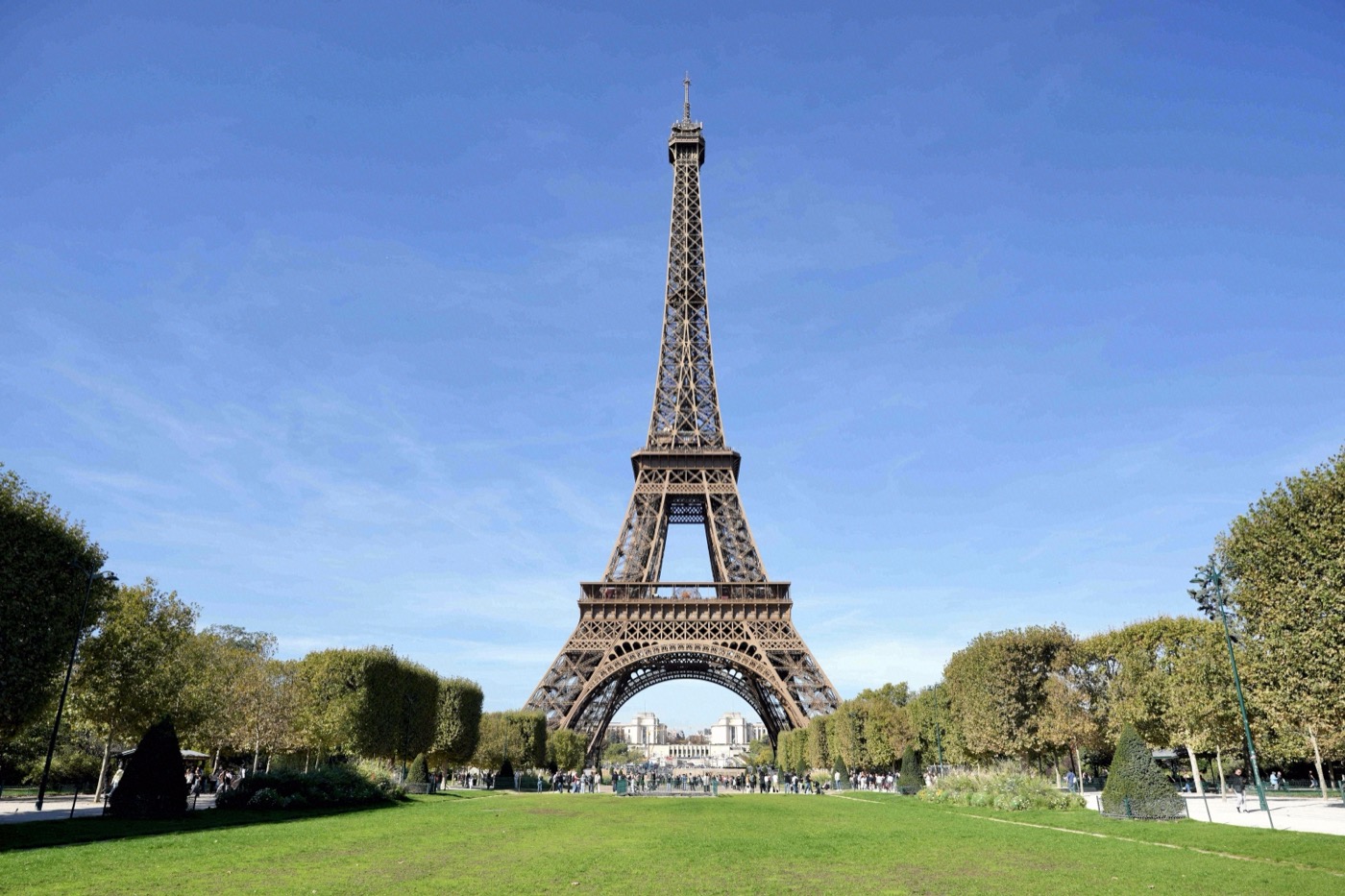 Der Eiffelturm ragt vor strahlend blauem Himmel über den grünen Wiesen des Champ de Mars empor.