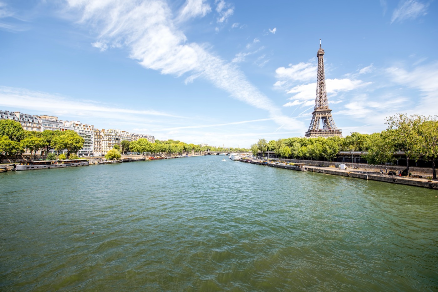 Weitwinkelaufnahme der Seine in Paris mit dem Eiffelturm im rechten Bildhintergrund, grünen Bäumen an den